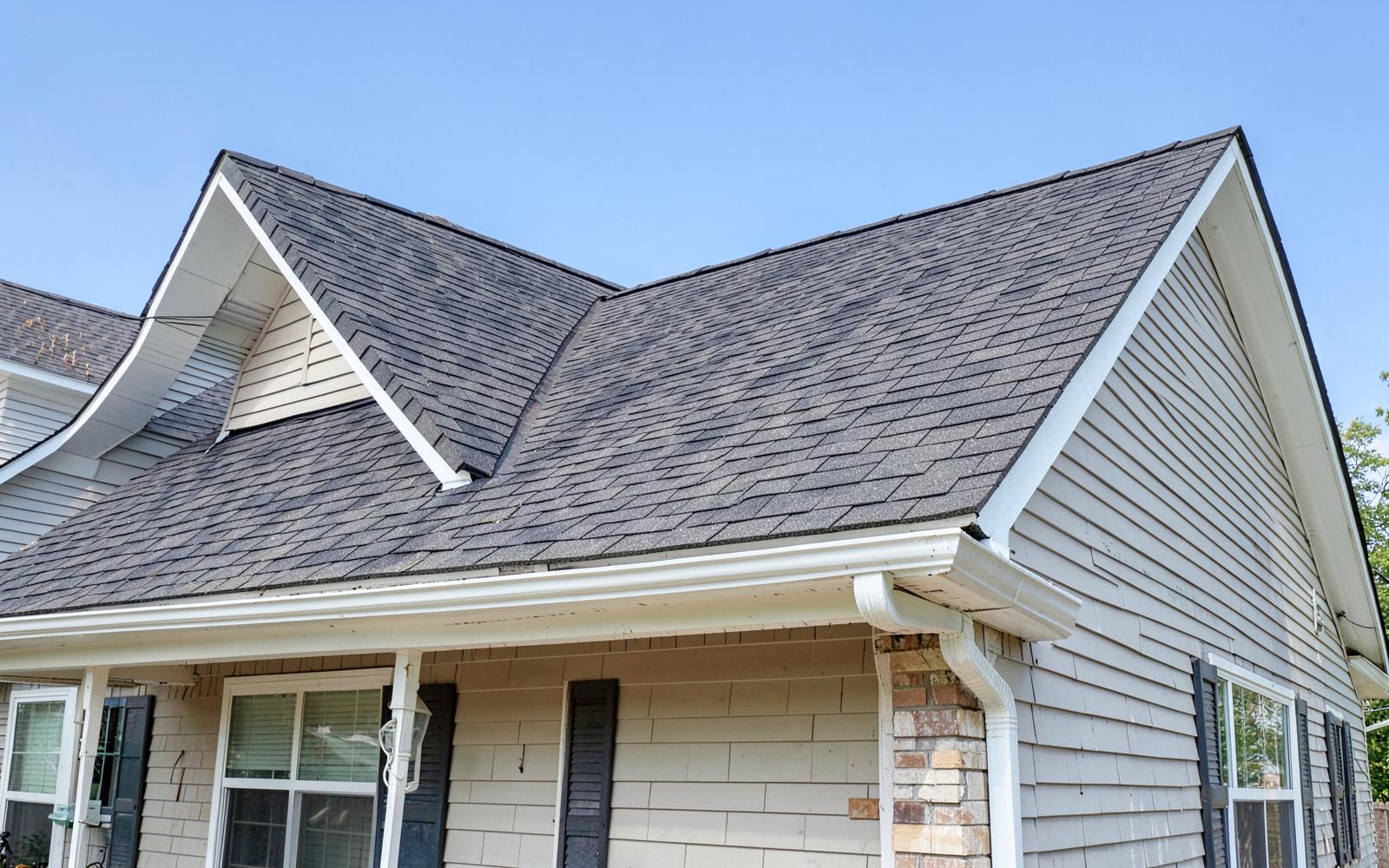 Newly installed asphalt shingle roof and white gutters on a suburban house